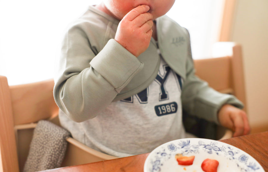 Baby self-feeding with mitten cuff scrunched back and hands free