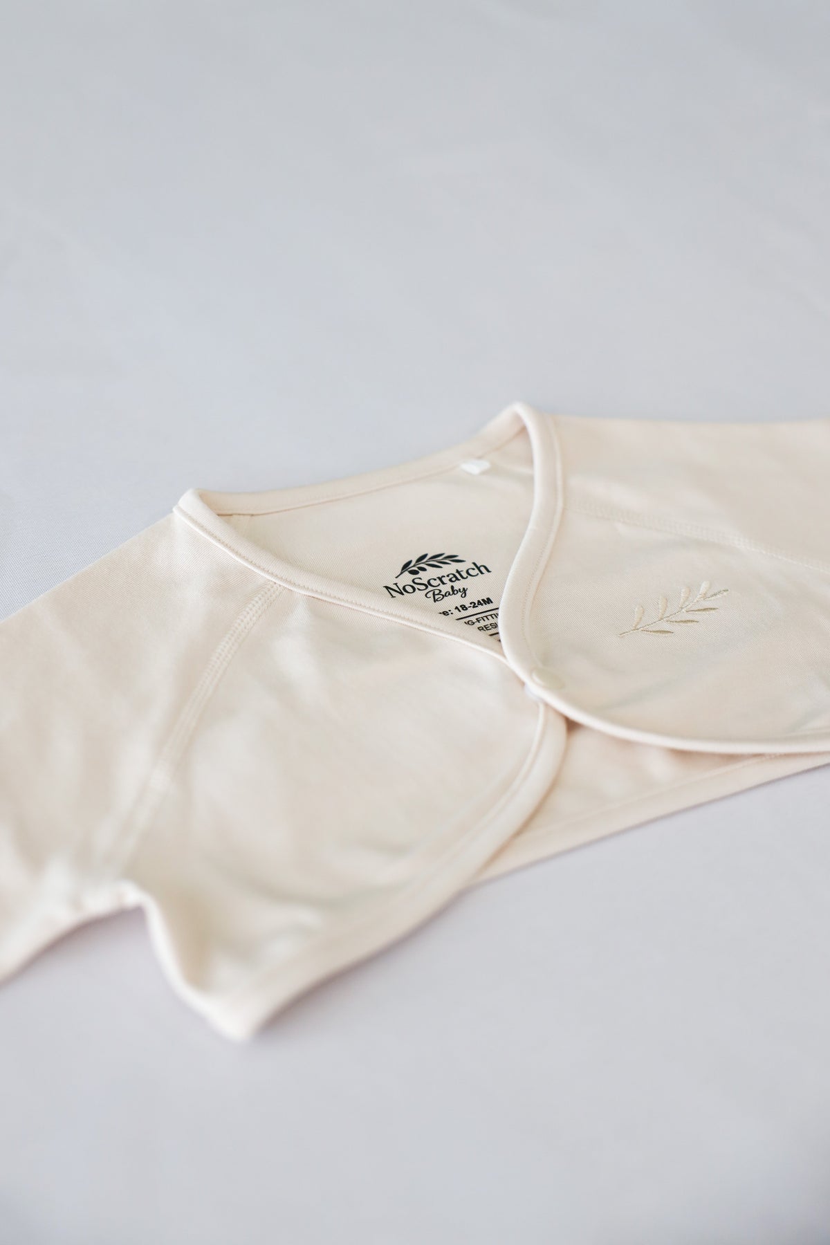 NoScratch Baby label and olive branch emblem detail on beige sleeve